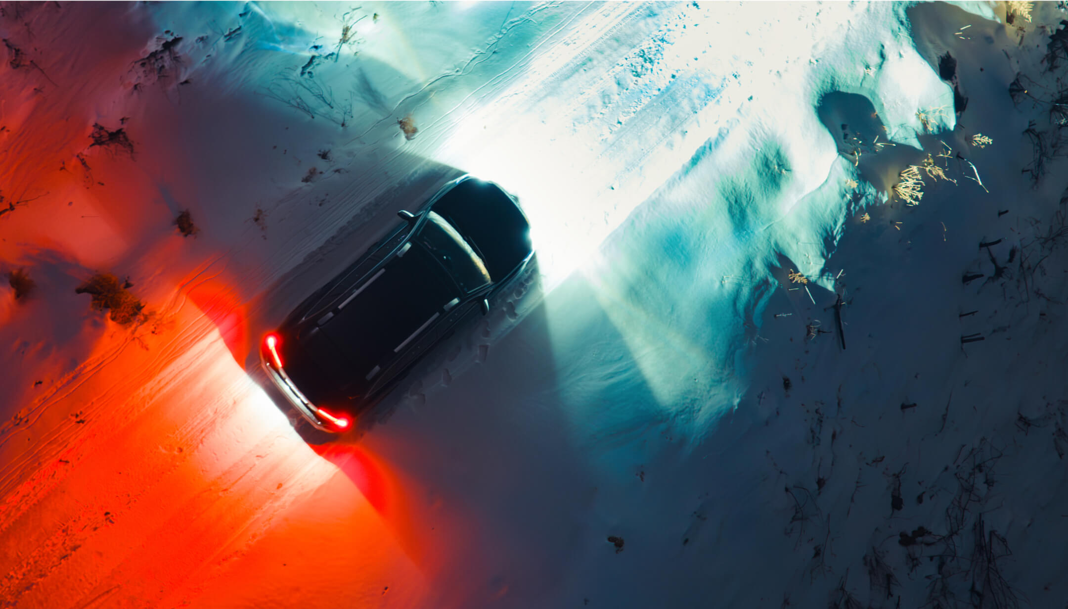 Aerial view of the snowy exterior with a car having its front and rear headlights on