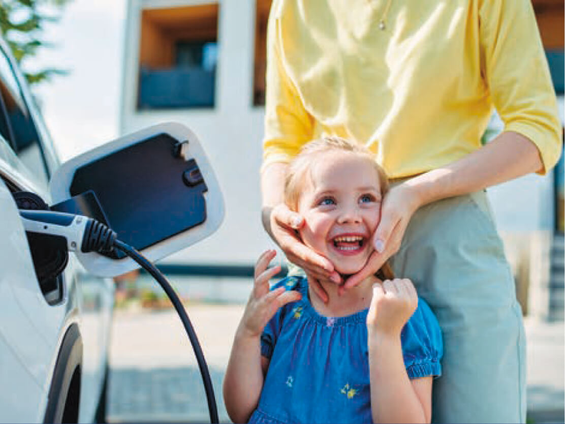 A woman caressing the face of a girl next to an electric vehicle charging