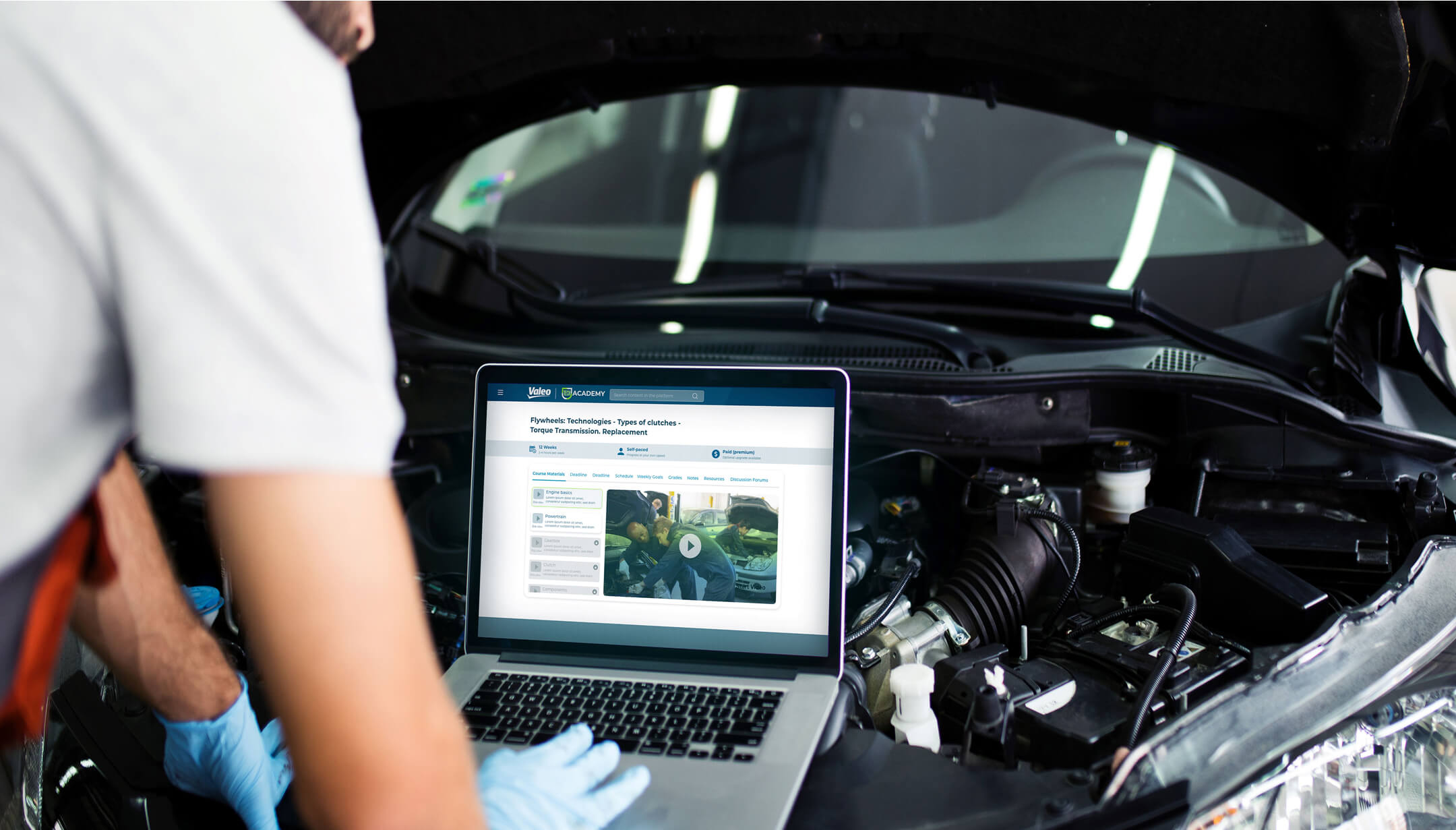 A technician in front of a car hood performing a diagnostic using a computer